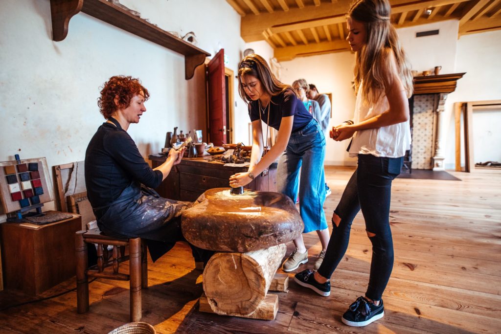 Een foto van een vrouw die 2 kinderen helpt met potten maken.