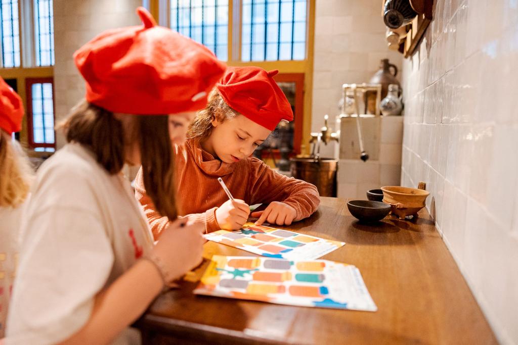 Kinderen zitten te verfen en hebben een baret op