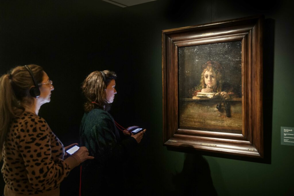 2 bezoekers kijken en luisteren naar het Titus schilderij